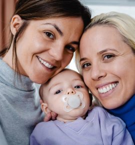 Gay lesbian couple and newborn baby taking selfie picture indoors at home - Lgbt family concept - Focus on left mother face
