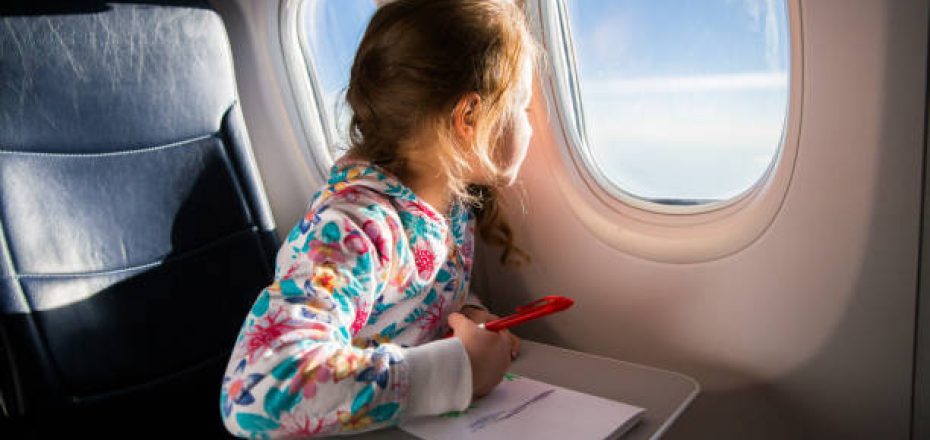 Child drawing picture with crayons in airplane. Little girl occupied while flying in aircraft. Travel with family and kids. Blue sky and sun outside the window
