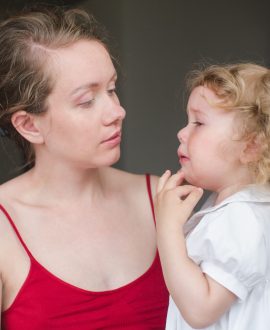 Young woman holding a sad child and looking at her. Horizontal indoors shot.